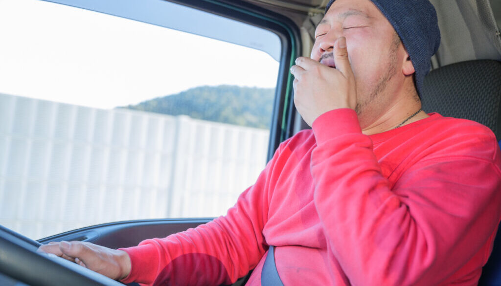 Male driver driving heavy truck while yawning